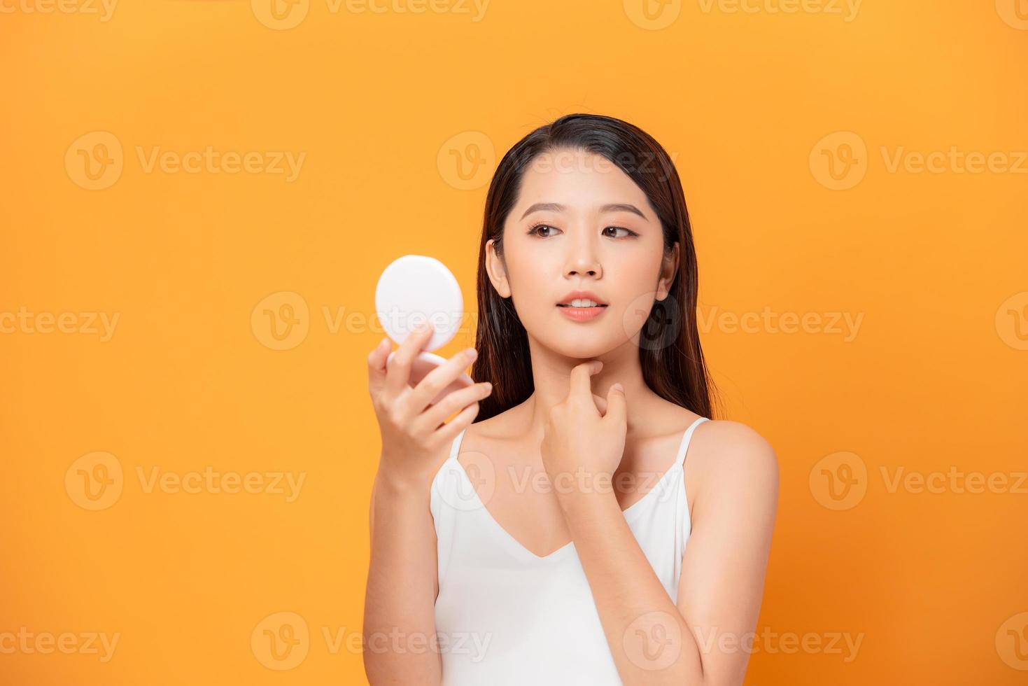 My skin feels great. Shot of a beautiful young woman looking at herself in small mirror over yellow isolated background photo