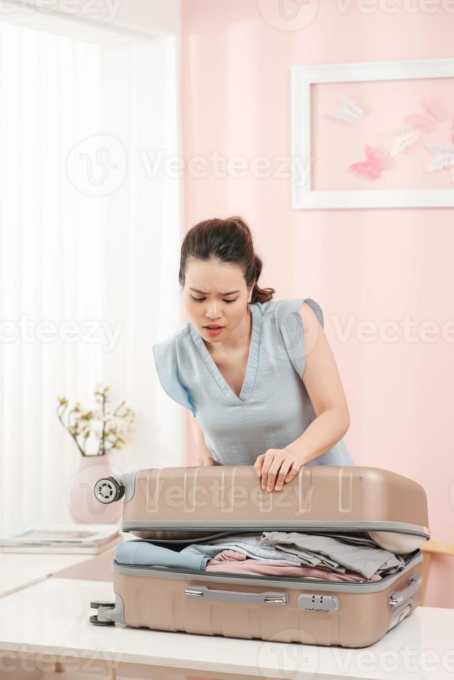 mujer prepara maleta de viaje en casa. mujer emocionada tratando de cerrar la maleta llena. foto