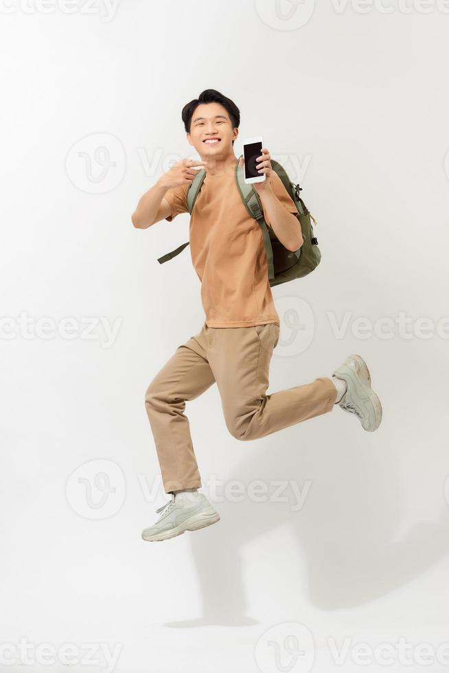 Portrait a smiling young man jumping isolated over white background, holding mobile phone, pointing finger photo