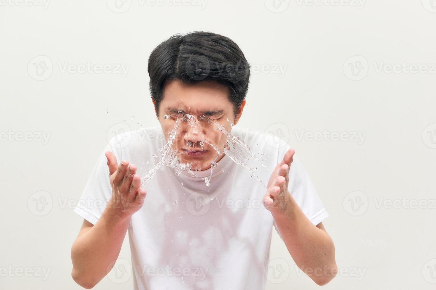 Young man spraying water on his face over white background photo