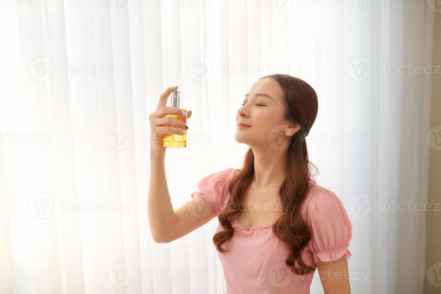 Girl with perfume, young beautiful woman holding bottle of perfume and smelling aroma. photo