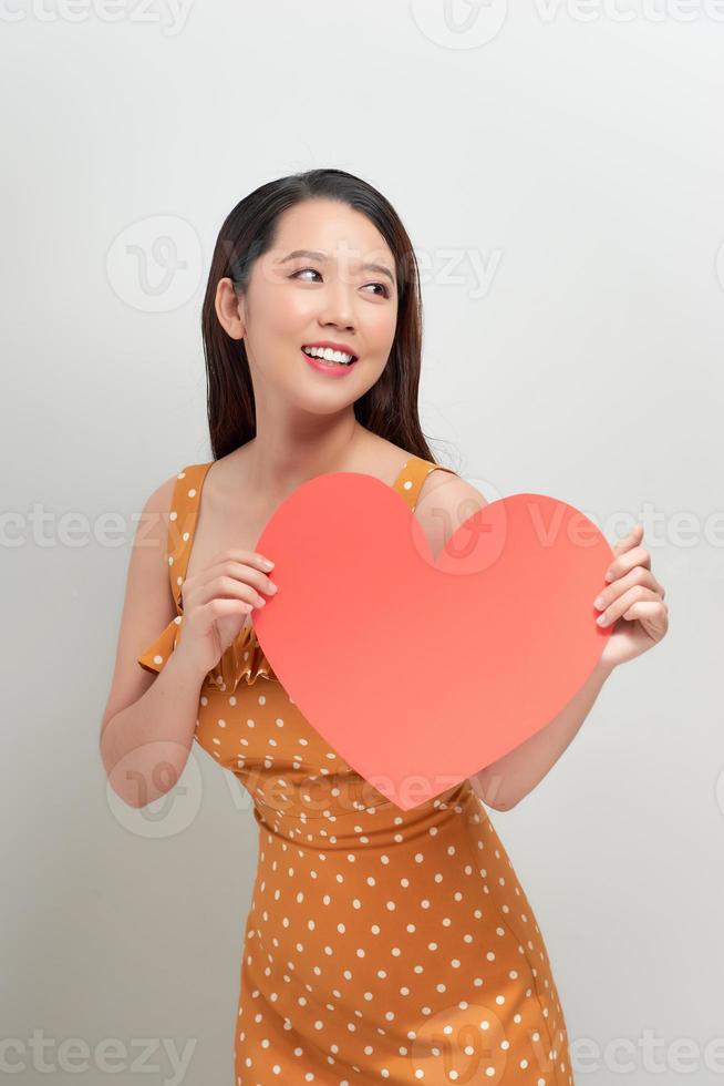 Lifestyle and Holiday Concept - Portrait Young happy woman in polka dot dress holding big red heart paper. photo