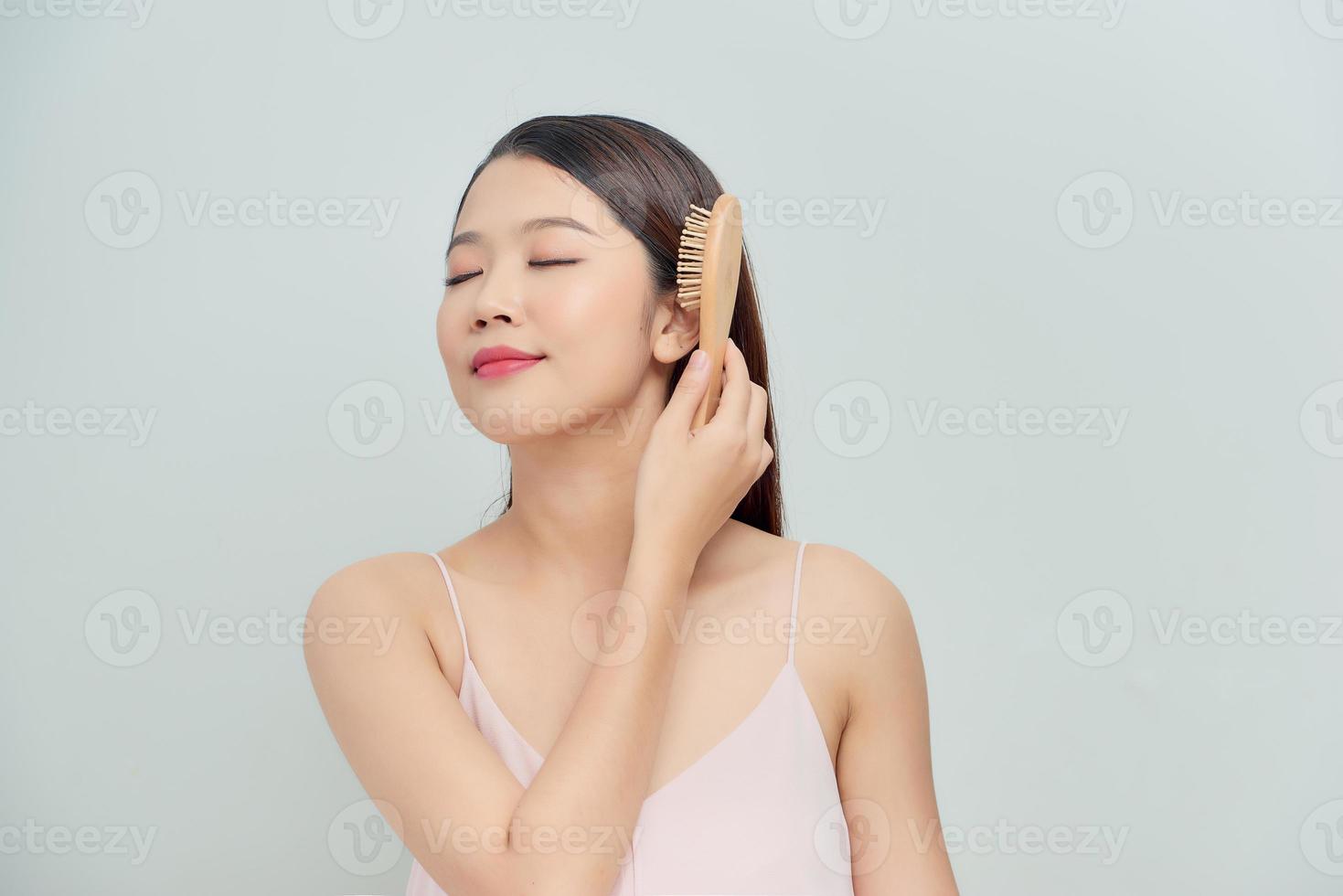 una mujer encantadora y hermosa con una sonrisa radiante se está cepillando el pelo largo foto