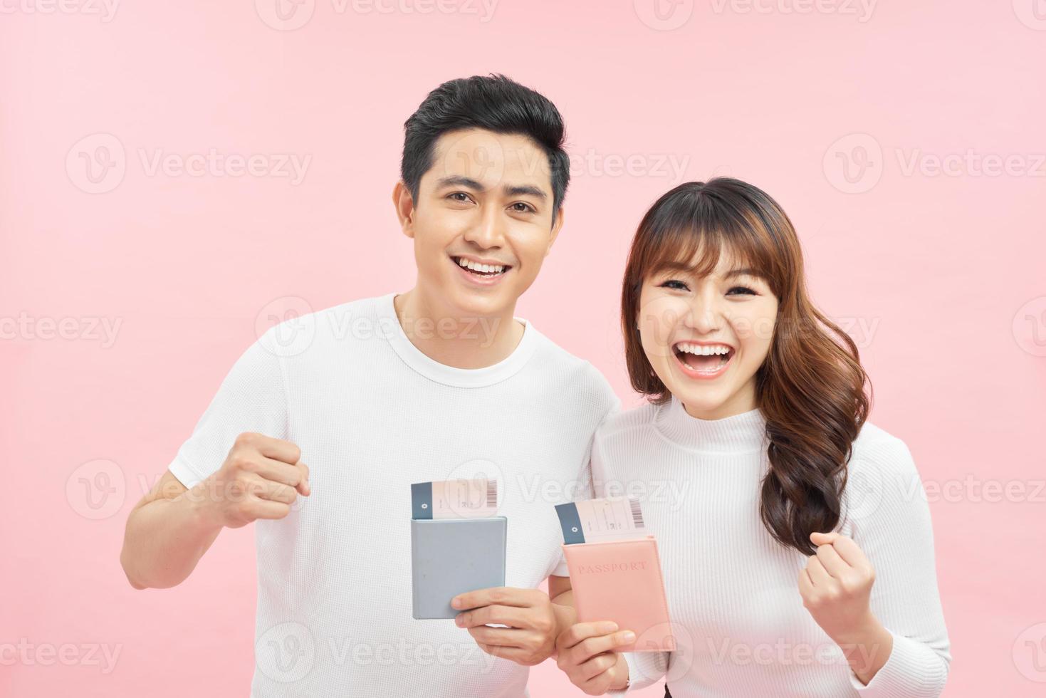 Portrait of successful lucky couple getting visa abroad holding raised fist showing passport with flying tickets shouting with wide open mouth isolated on pink background photo