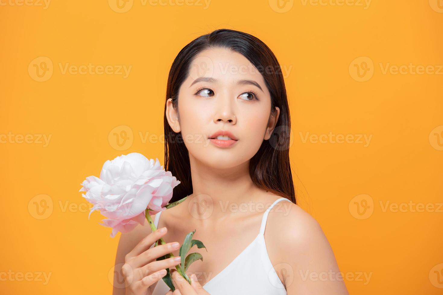 beautiful young woman with pink flower isolated on yellow photo