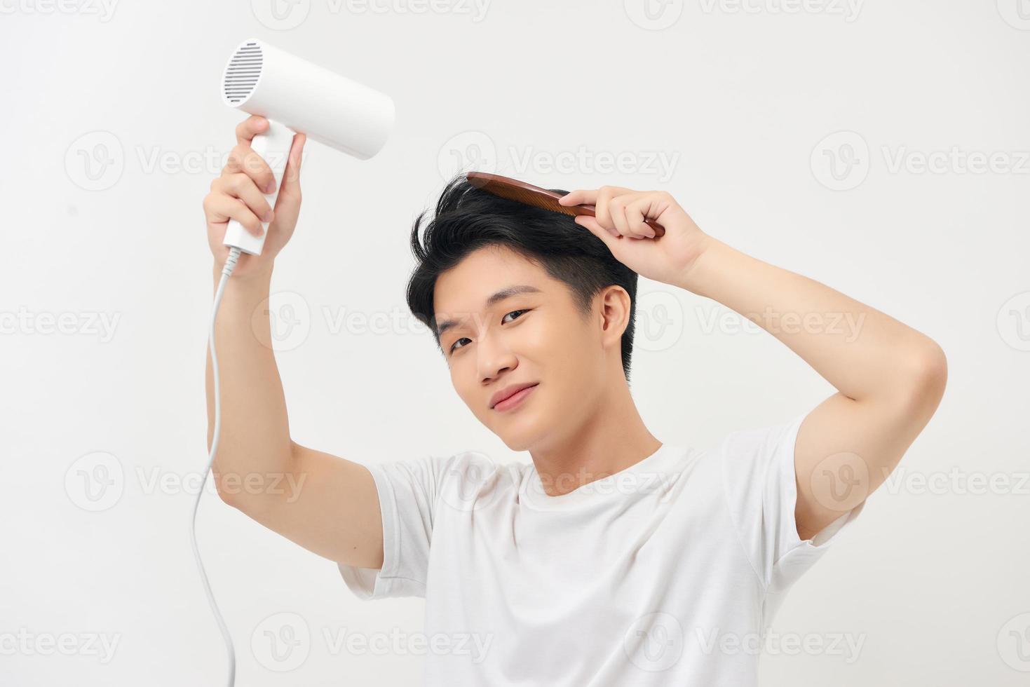 apuesto joven secándose el pelo y sonriendo mientras está de pie contra el fondo blanco foto