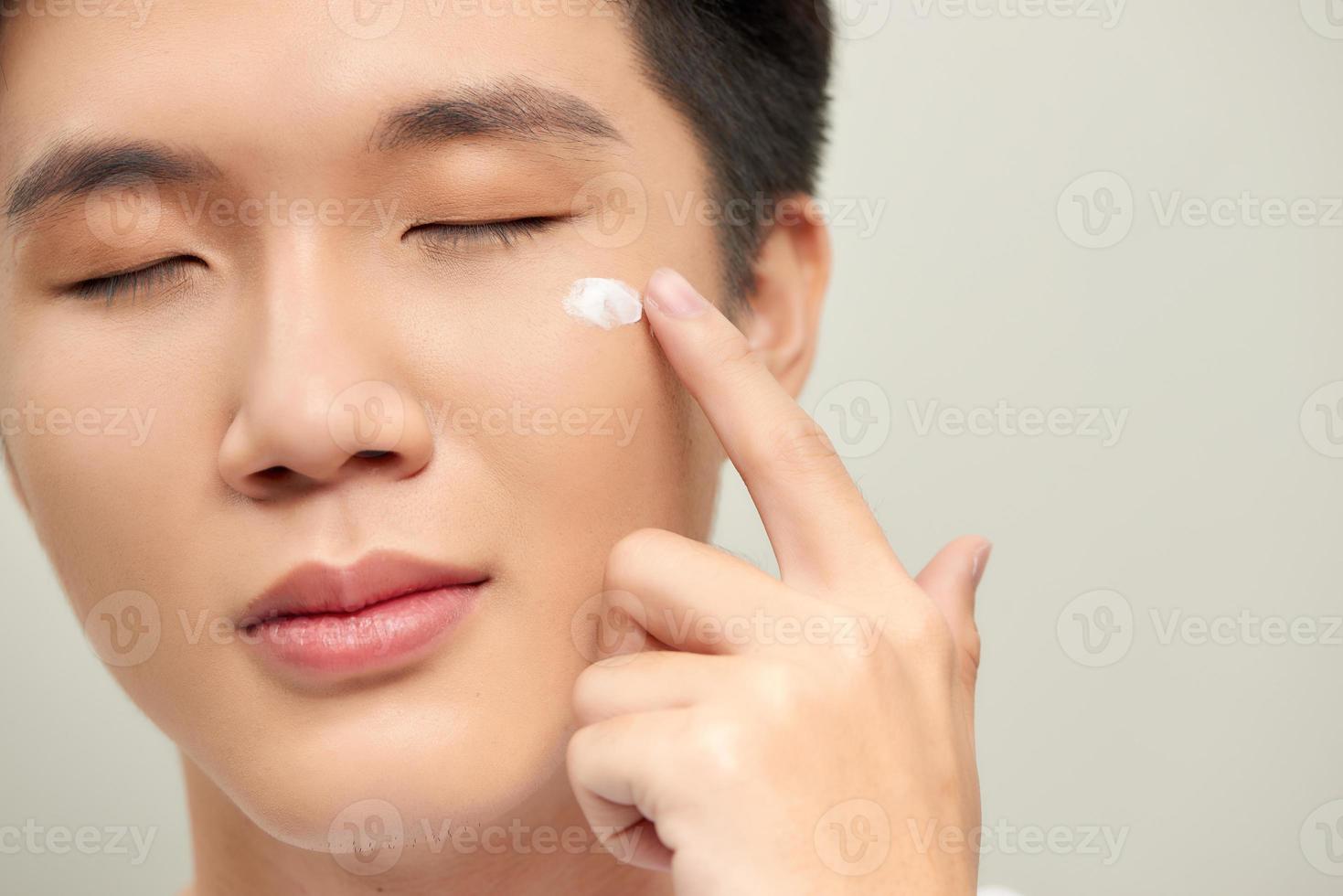 Handsome man applying eyes cream close up portrait studio on white background photo
