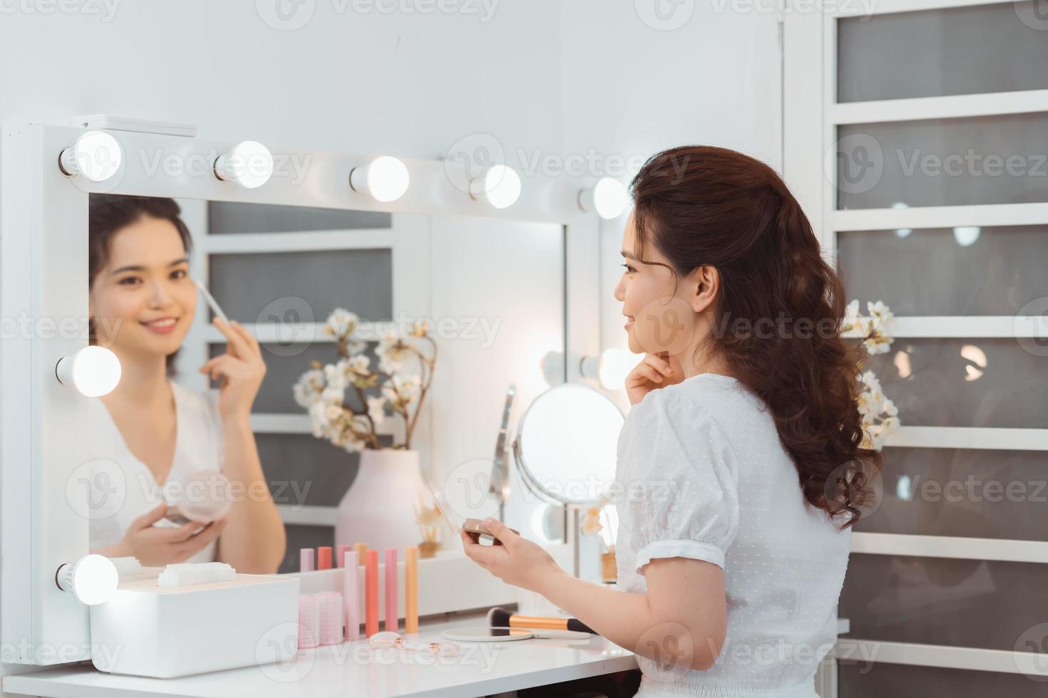 Young stylish woman applying makeup by eye shadow brush in mirror photo