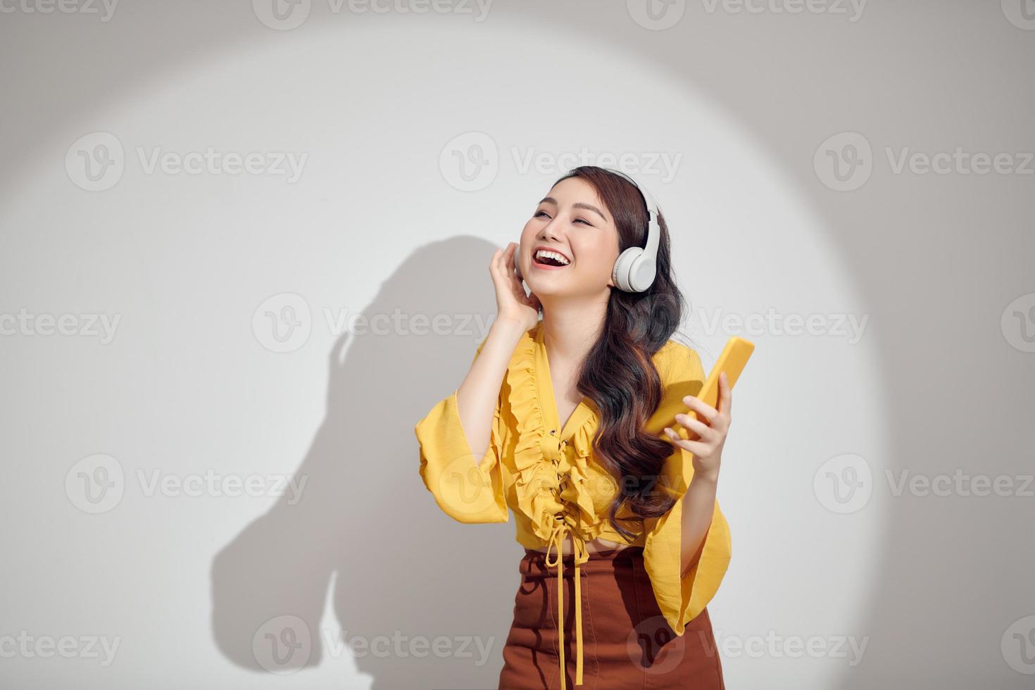 mujer despreocupada encantada al ritmo de la melodía, escucha una canción fuerte en los auriculares, sostiene el teléfono inteligente y se divierte foto