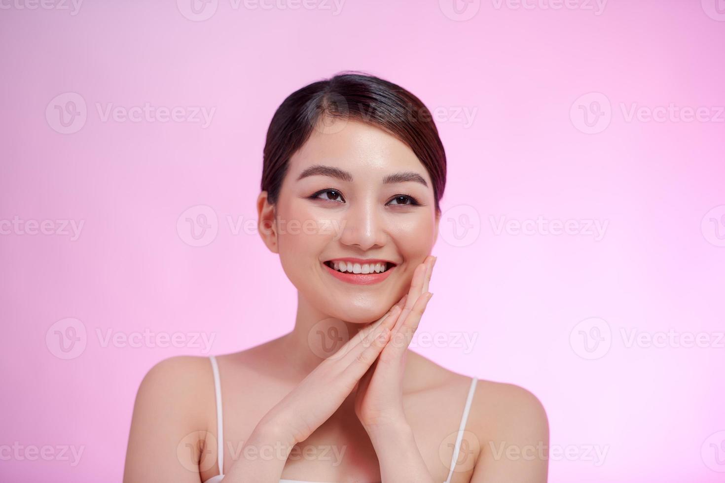 hermosa mujer asiática tocando una suave sonrisa en la mejilla con piel limpia y fresca con emociones positivas sobre fondo blanco foto