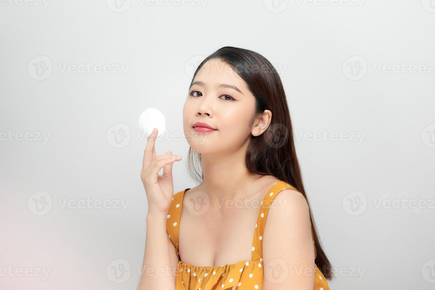 foto de una hermosa joven mujer bastante asiática con piel sana posando desnuda aislada sobre fondo de pared blanca sosteniendo toallitas de algodón.