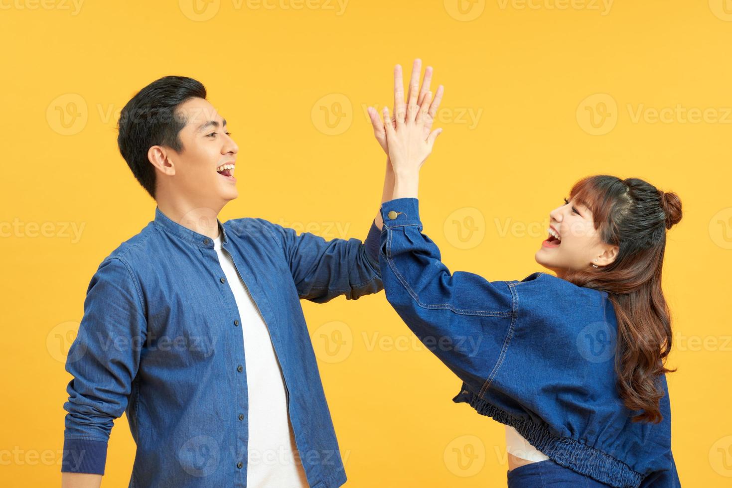 Positive young couple give high five, agree to work as team, stand sideways, isolated on yellow wall. Male student with notepad touches palm of girlfriend, have agreement. photo