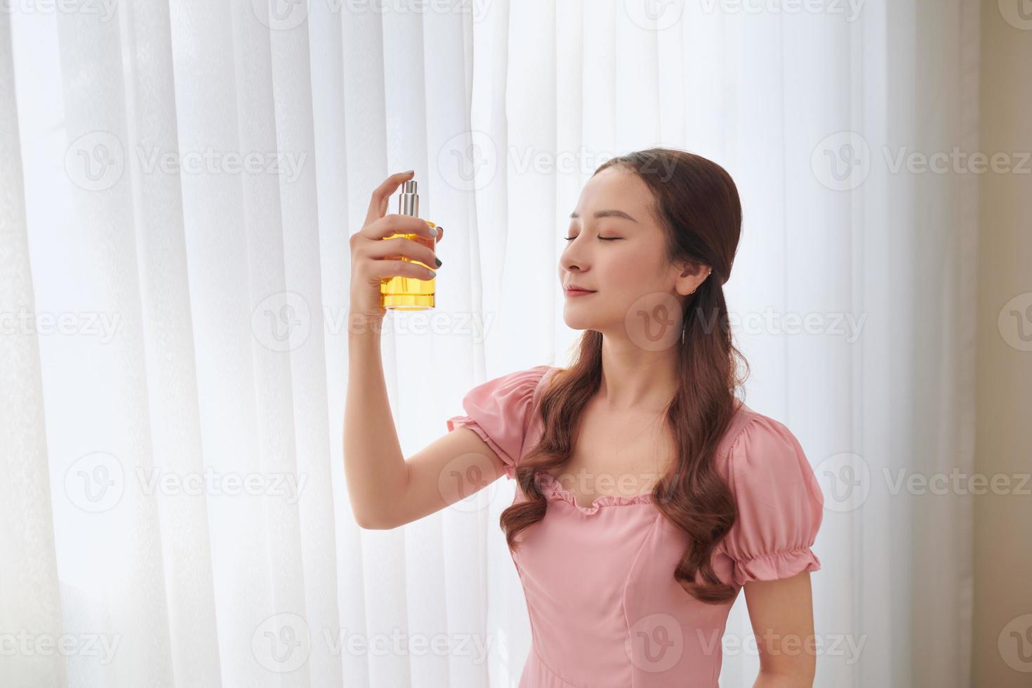 Girl with perfume, young beautiful woman holding bottle of perfume and smelling aroma. photo