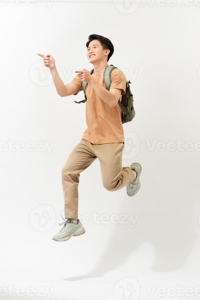 Young cheerful energetic handsome Asian man jumping with hands pointing to copy space aside  isolated on white background photo