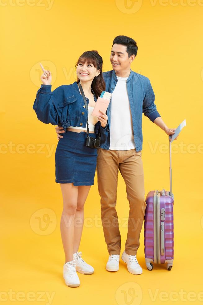 young travelling couple with suitcases pointing somewhere isolated on yellow photo
