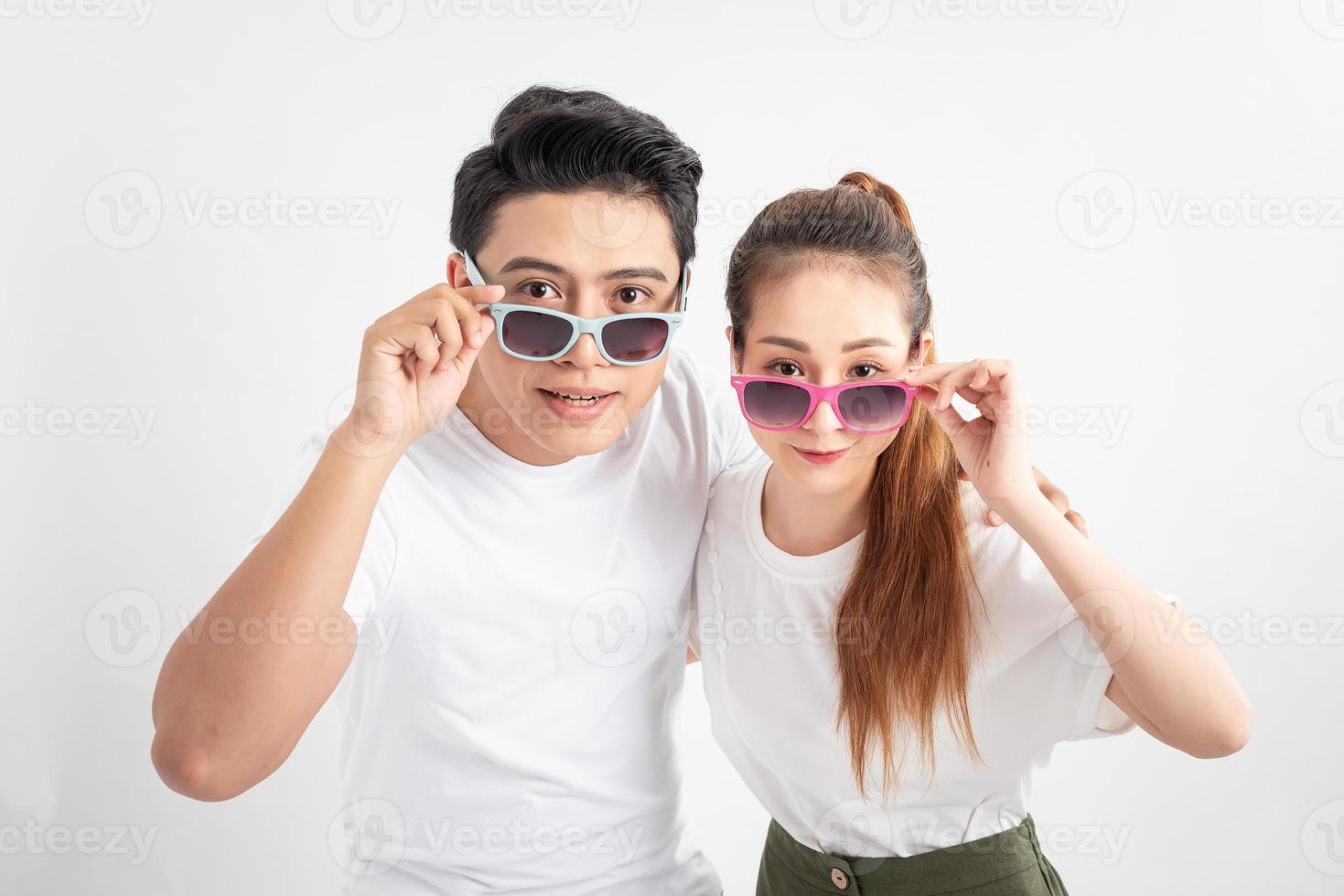 Beautiful cute adorable surprised couple putting colorful spectacles down showing wow emotion over yellow background, isolated photo