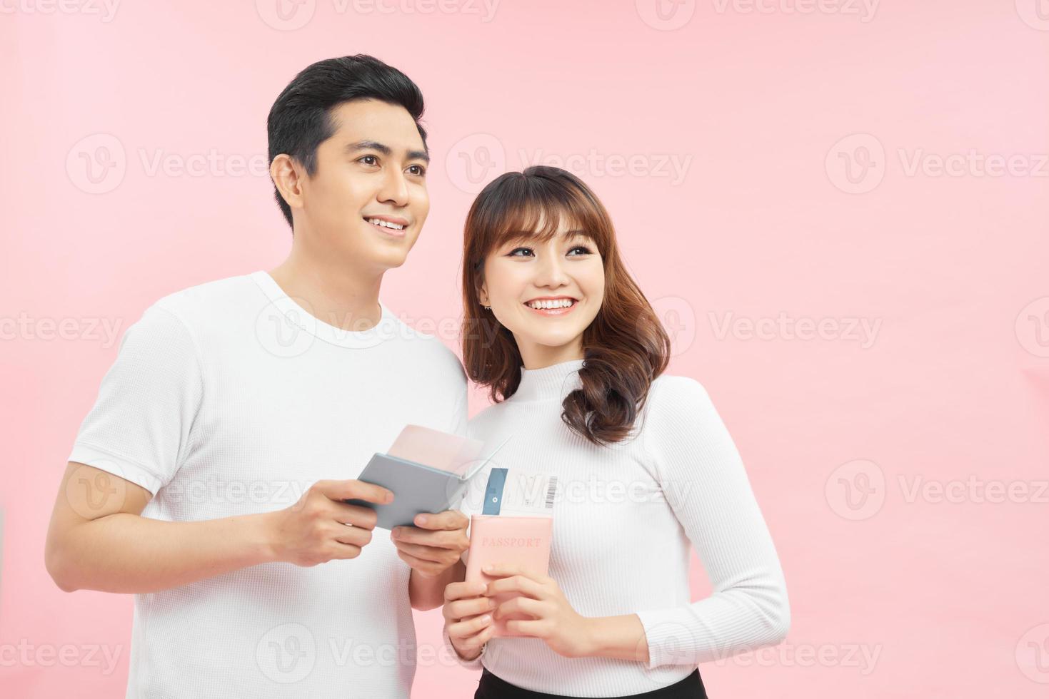 Portrait of an attractive cheerful young couple  standing isolated over pink background, showing passport with flight tickets photo