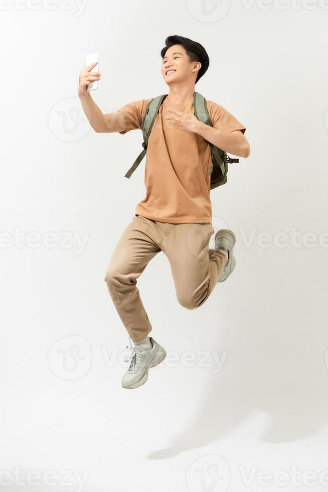 Full length portrait of a smiling young man taking a selfie while jumping isolated over white background photo