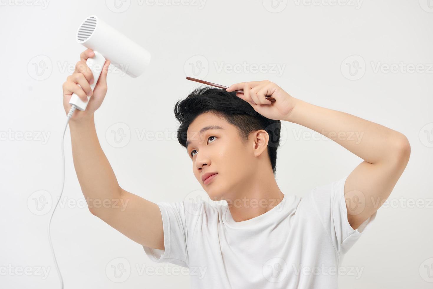 joven guapo secándose el pelo aislado en blanco foto