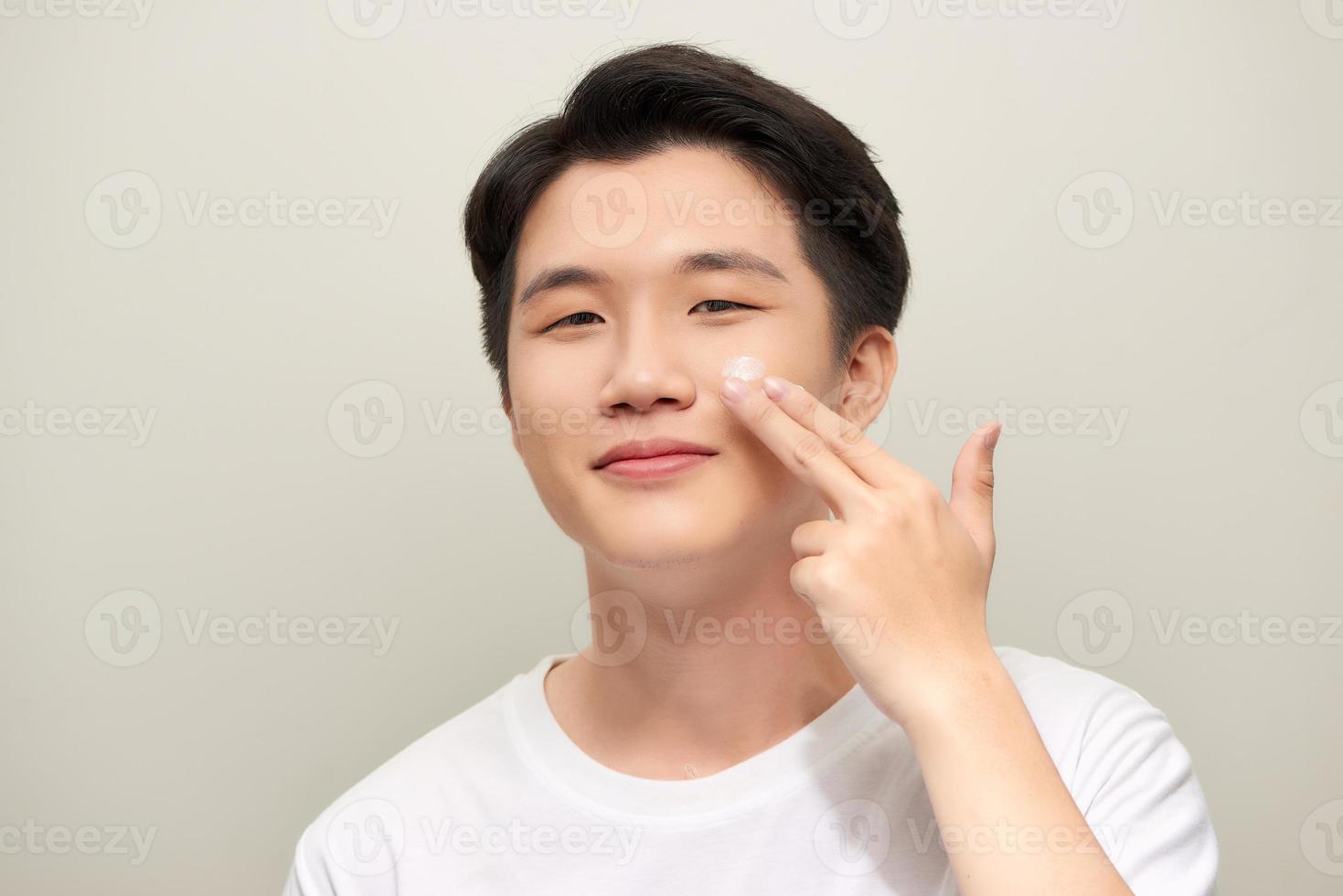 Handsome man applying eyes cream close up portrait studio on white background photo