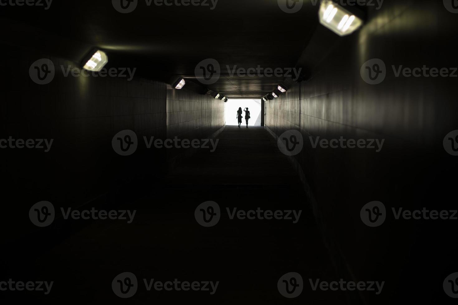 Two silhouettes at end of tunnel. Light in distance. Figures of small women in contrasting light. photo