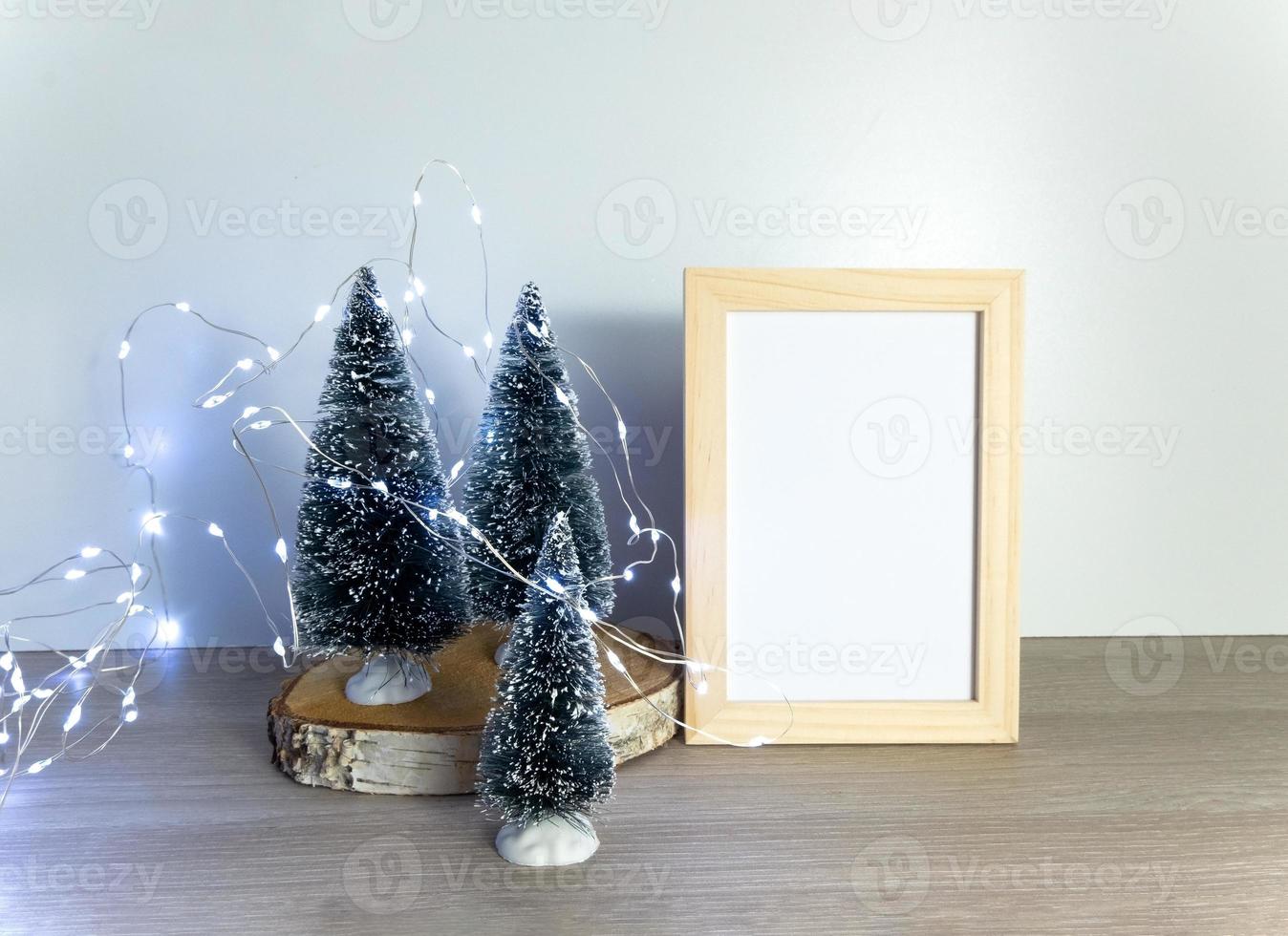 Christmas arrangement, little fir tree, blank photo frame, lights garland, festive composition with copy space for artwork presentation, mockup, winter holidays decor, selective focus