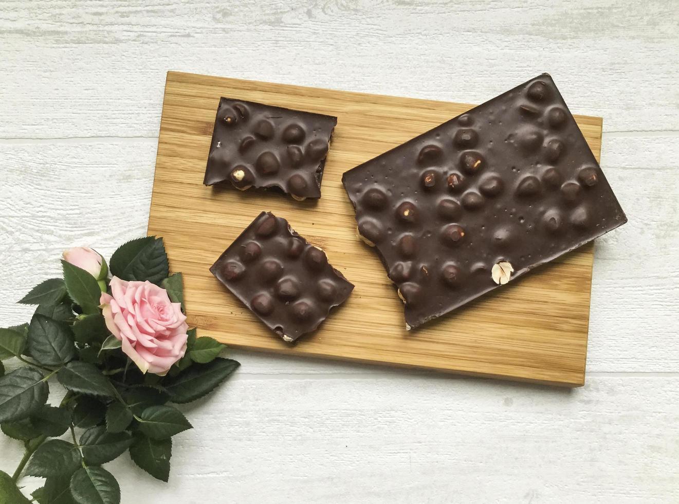 flat lay, broken chocolate bar on the wooden board and a pink rose photo
