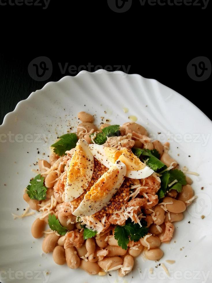 Fish and bean salad with an egg on a black background. photo