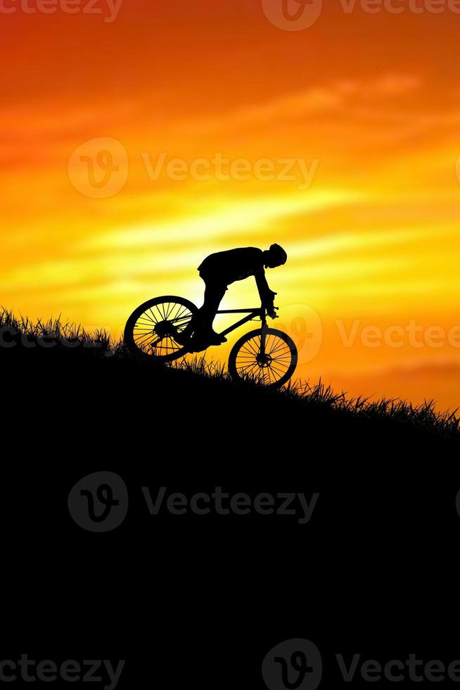 A silhouette of a cyclist descending from the mountain in the evening. photo