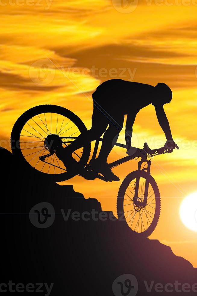 A silhouette of a cyclist descending from the mountain in the evening. photo