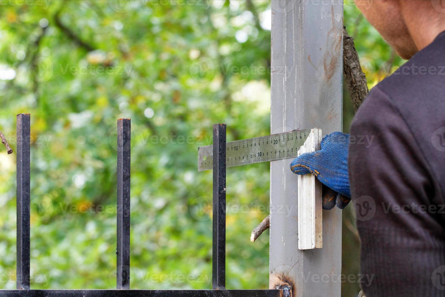 un trabajador mide el grosor con un cuadrado y pone marcas en un poste de cerca de metal. foto