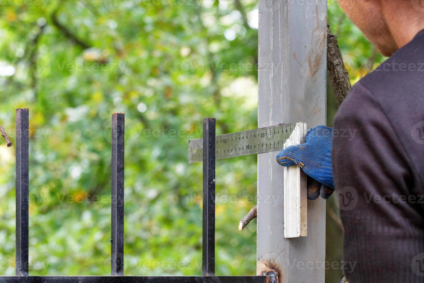 A worker measures the thickness with a square and puts marks on a metal fence post. photo