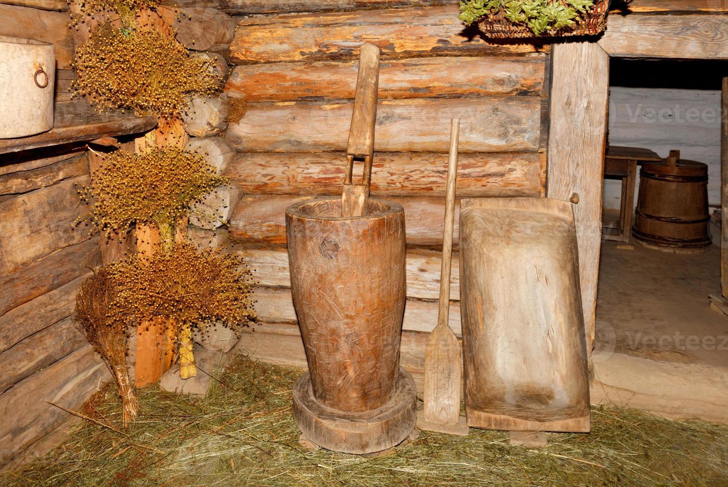 A wooden mortar, a shovel for the stove and a trough in the hallway of an old rural log hut near tied bouquets of flax. photo