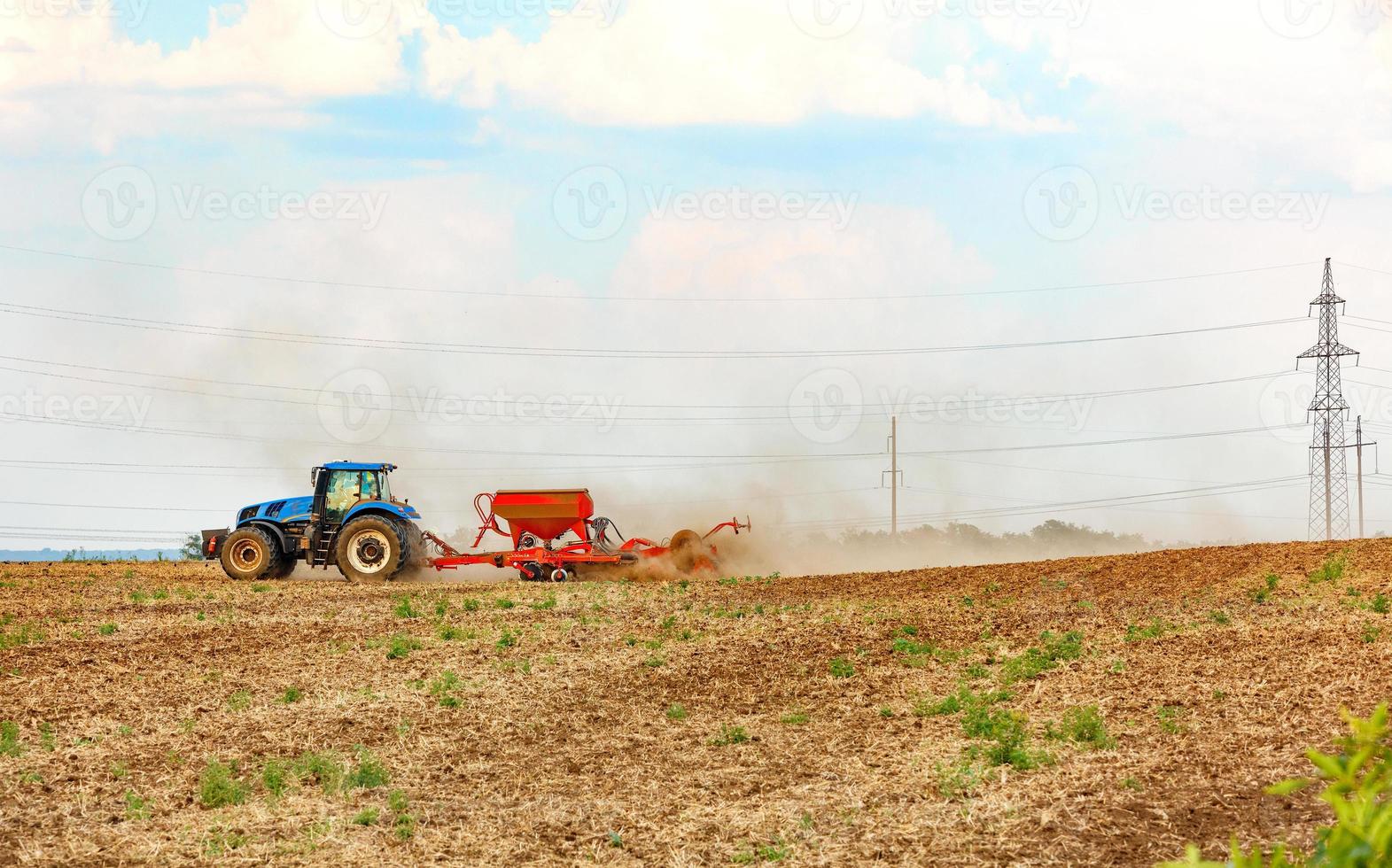 An agricultural tractor with a trailed seeder cultivates the soil in the field by applying the necessary fertilizers. photo