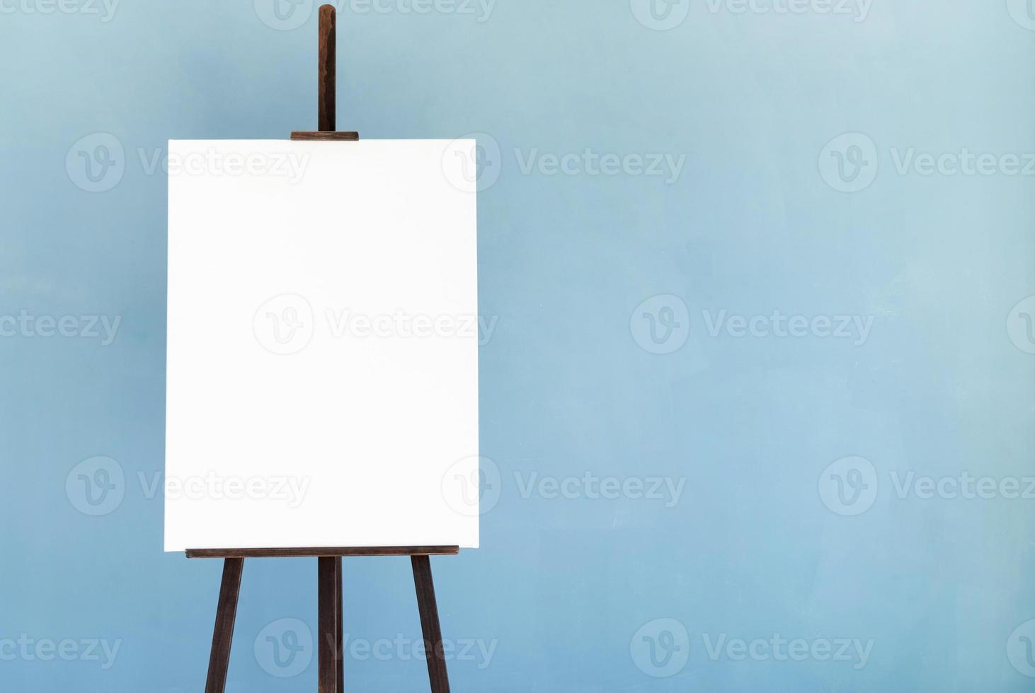Wooden easel with blank canvas on light blue background for mockup design photo