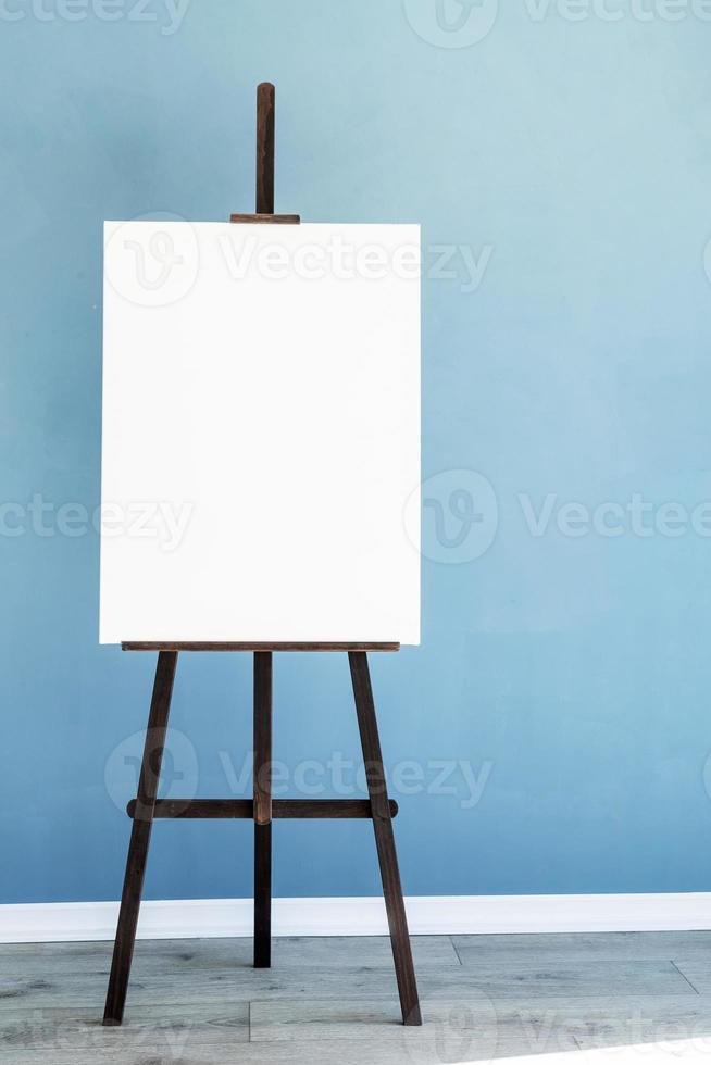 Wooden easel with blank canvas on light blue background for mockup design photo