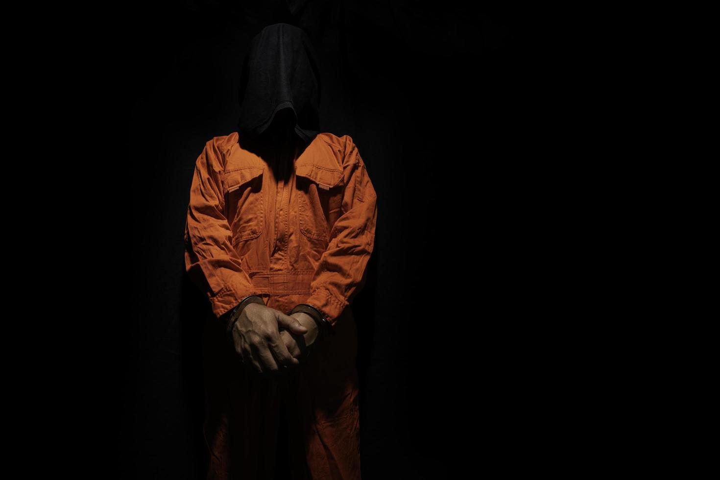 Handcuffs on Accused Criminal in Orange Jail Jumpsuit. Law Offender Sentenced to Serve Jail Time, in black background photo