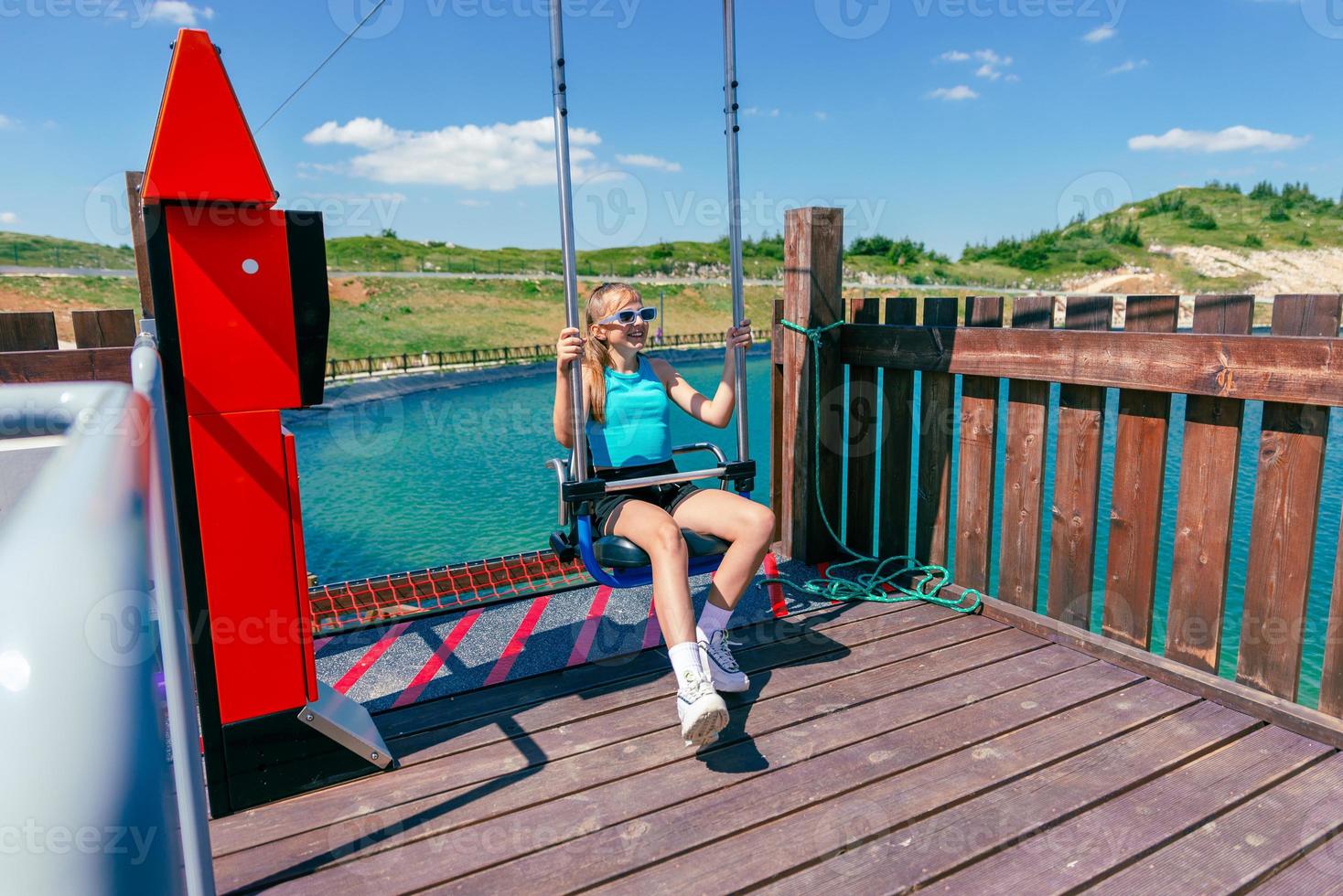 chica llega en una silla de paracaidismo en un parque de aventuras de montaña. lago de fondo foto