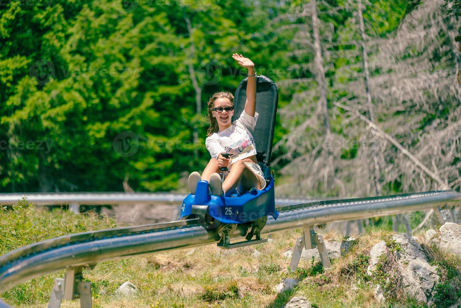 Girl rides a mountain roller coaster and waves. Mountain environment with trees in the background photo