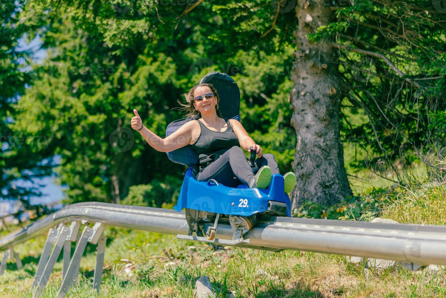 Woman with sunglasses rides a mountain roller coaster with a thumbs up. Warm summer day on the mountain photo