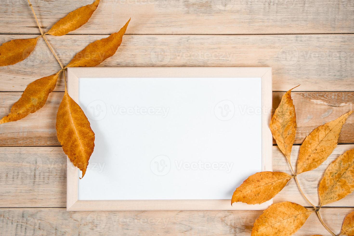 Hello autumn concept. Empty frame mock up on wooden background and yellow fallen leaves. photo