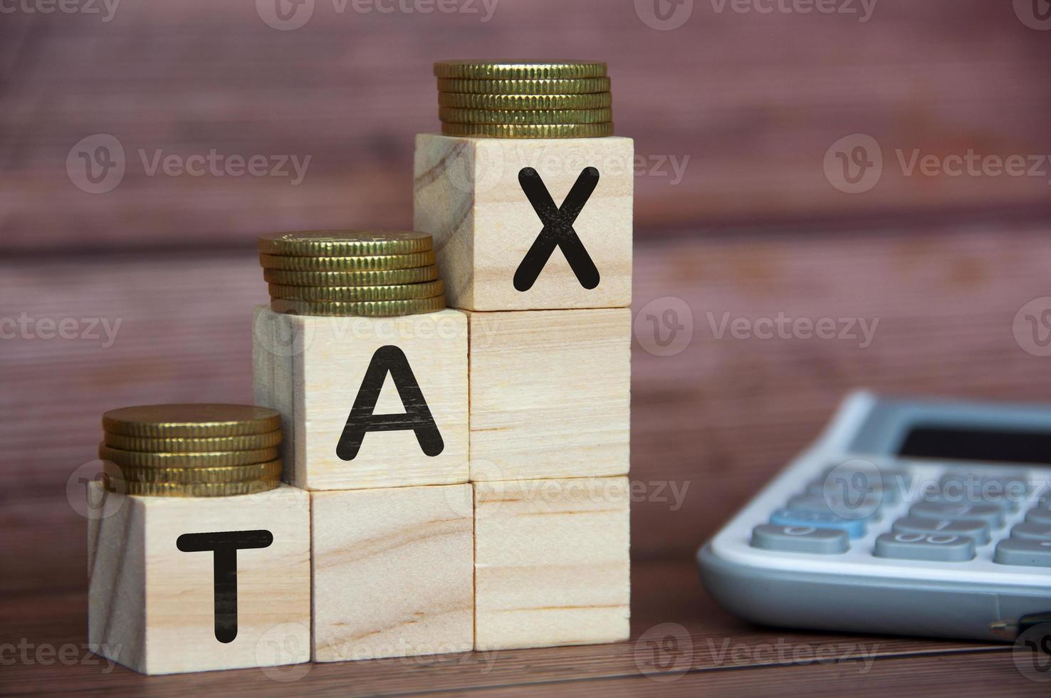 Tax word on wooden blocks with gold coins on top and calculator background. Tax concept photo