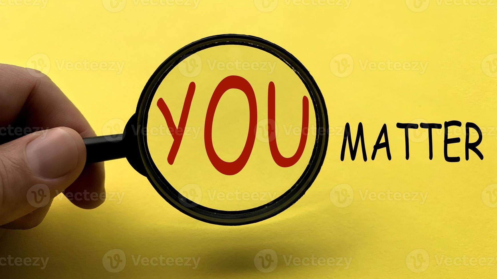 Hand holding magnifying glass with text You matter on yellow cover background. Motivational concept photo