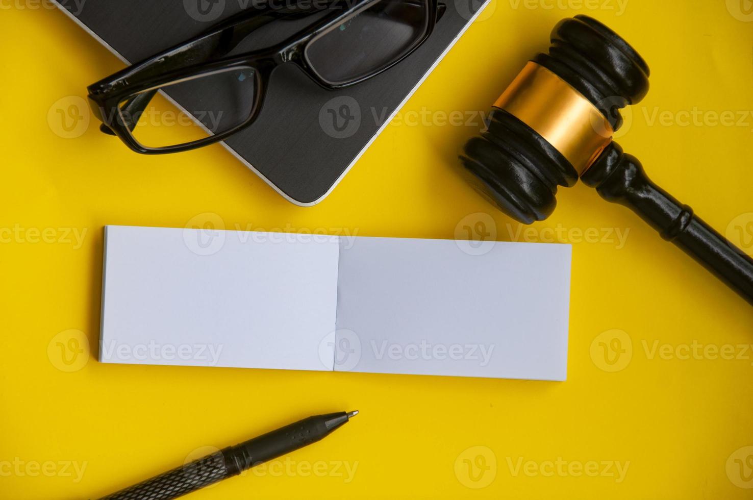Top view of blank paper note with gavel, laptop, glasses and pen on yellow background. photo
