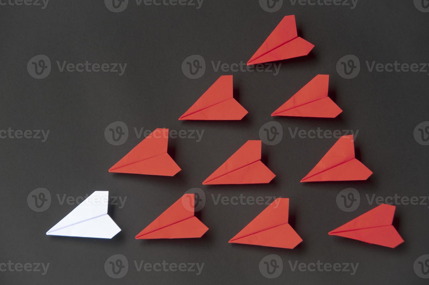 origami de avión de papel blanco liderando planos rojos sobre fondo oscuro. concepto de habilidades de liderazgo foto