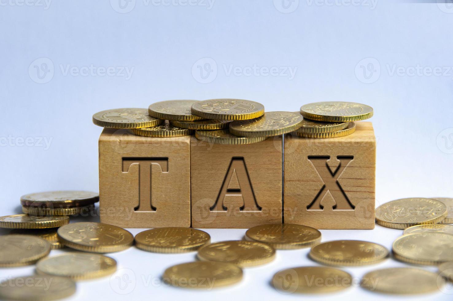 Tax word engraved on wooden block surrounded with gold coins. Taxation concept photo
