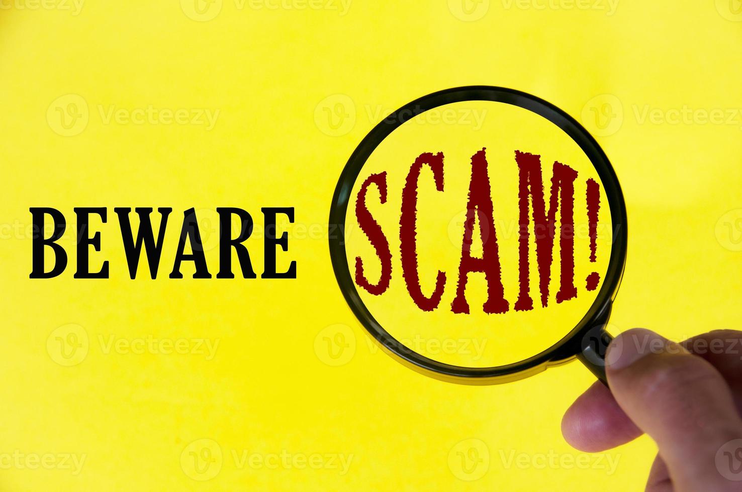 Beware scam text on yellow cover with hand holding magnifying glass. Scamming and fraud concept photo