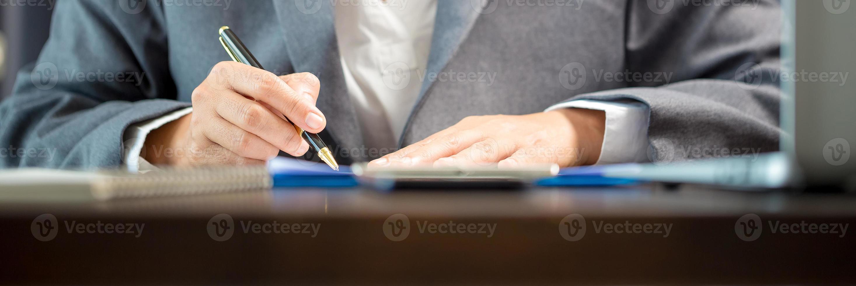 Workplace closeup person professional businesswoman sitting at desk hold pen signing or signature contract paper. Employee woman writing agreement document on paperwork form corporate at work office photo