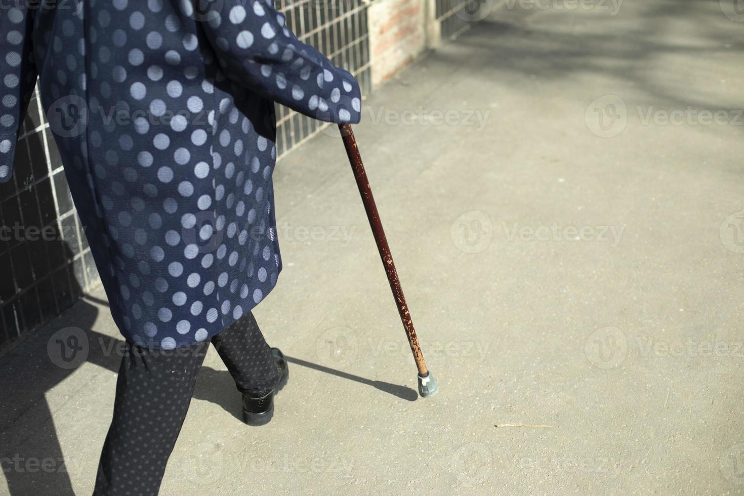 Grandma with walking stick. Woman walks on asphalt. photo