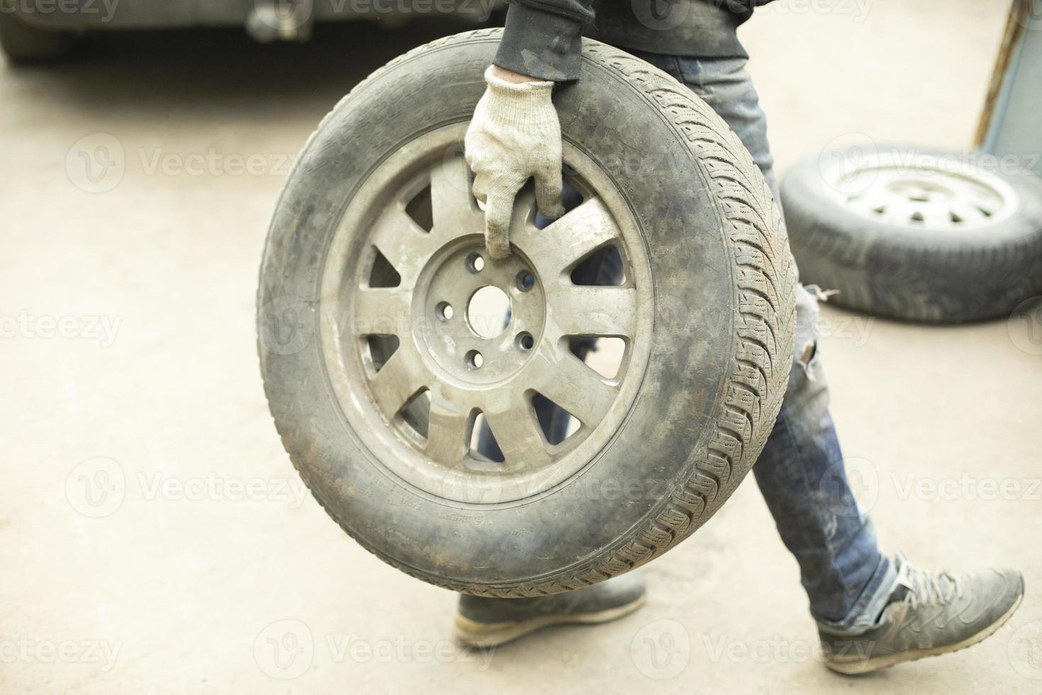 Guy changes wheel. Man carries wheel from car in his hand. Person makes tire service. photo